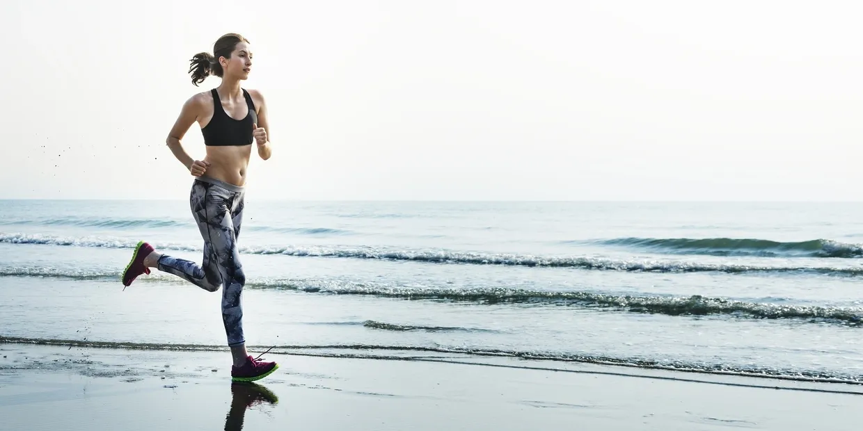 A woman is running on the beach near water.