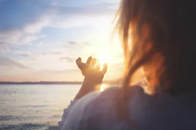 A woman is holding her hand out to the sun.